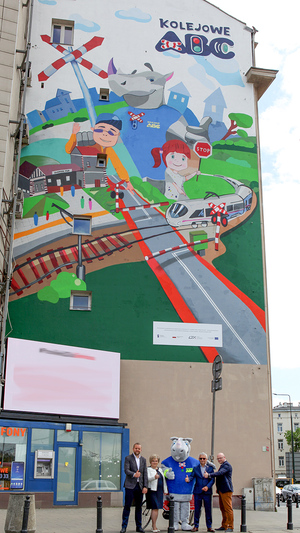 Cztery osoby wraz z rogatkiem na tle muralu Kampanii Kolejowe ABC