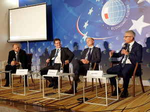 Dyskusja podczas Forum: czterej mężczyźni siedzą na podium, jeden z mikrofonem