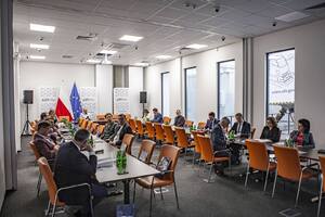 Wnętrze sali konferencyjne z rozłożonymi stołami i krzesłami na których siedzą uczestnicy Sejmowej Komisji Infrastruktury