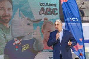 Wiceprezes UTK Marcin Trela podczas wystąpienia na Konferencji prasowej Kolejowego ABC II za nim baner kampanii Kolejowe ABC II