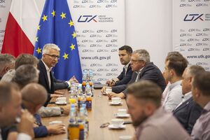 Po lewej stronie Prezes Urzędu Transportu Kolejowego dr inż. Ignacy Góra oraz Przedstawiciele Związku Zawodowego Maszynistów Kolejowych siedzący przy stole. W tle flaga Unii Europejskiej i flaga Polski.