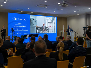 Wiceprezes UTK Kamil Wilde omawia prezentację na temat projektów UTK realizowanych we współpracy z CUPT i przy wsparciu środków UE. W tle niebieski ekran z logo CUPT częściowo wyświetlający prezentację.