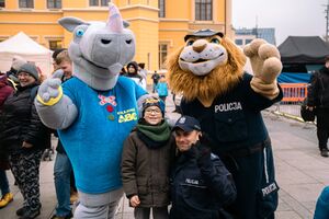 Nosorożec rogatek pozujący do zdjęcia wraz z dzieckiem i policjantem oraz maskotą policjanta. Nosorożec To osoba w przebraniu z głową nosorożca i niebieską koszulką