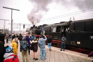 Zdjęcie peronu na peronie zgromadzone osoby. Osoby oglądają starą czarną lokomotywę parowozu.