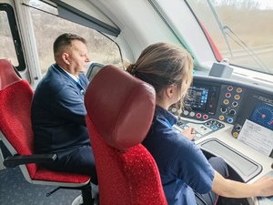 Wnętrze kabiny maszynisty. Za sterami pociągu siedzi kobieta obok niej siedzi mężczyzna.